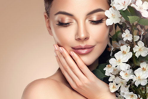 Beautiful young woman with clean fresh skin touching her face in flowers  . Girl facial  treatment   . Cosmetology , beauty  and spa . Female  model, care concept